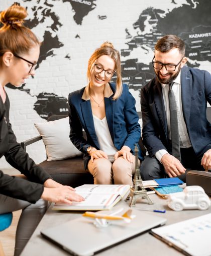 Young businesscouple choosing a trip with agent sitting at the travel agency office with world map on the background